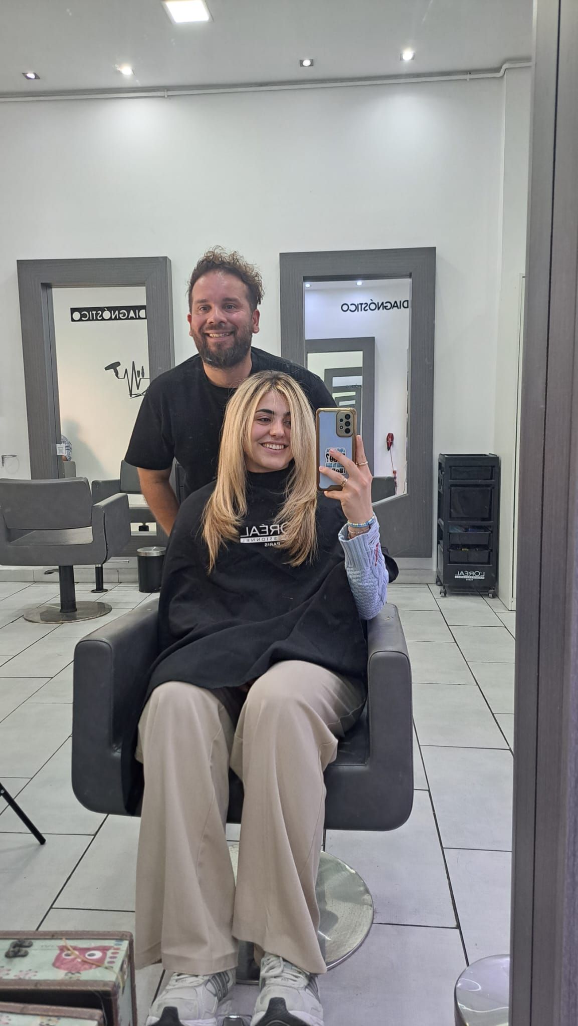 Una mujer está sentada en una silla frente a un espejo mientras un hombre está detrás de ella.