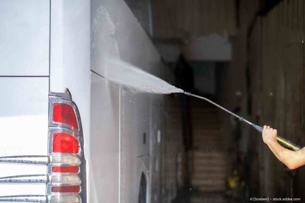 Eine Person bespritzt nachts einen weißen Lieferwagen mit Wasser aus einem Schlauch.