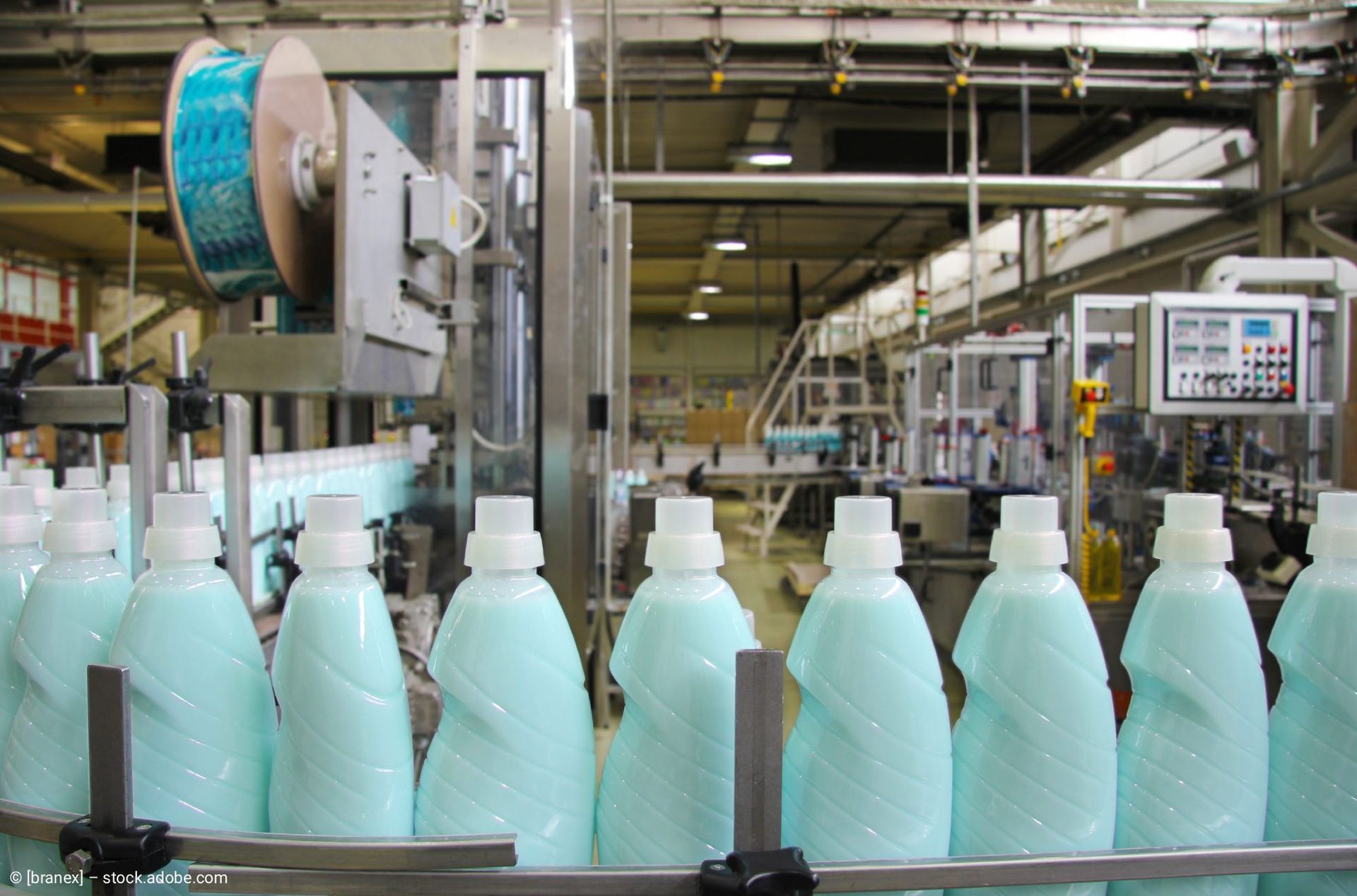 Eine Reihe durchsichtiger Plastikflaschen auf einer industriellen Abfüllanlage mit Maschinen im Hintergrund