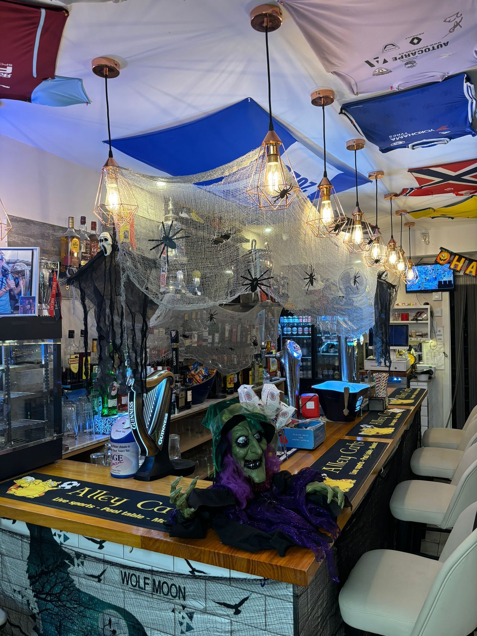 Un bar con una bruja en el mostrador y banderas colgando del techo.