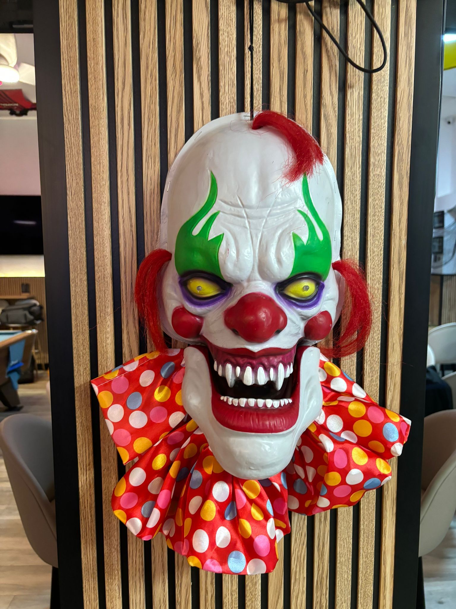 Una máscara de payaso está colgada en una pared de madera.