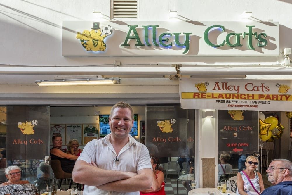 Un hombre está parado frente a un restaurante con los brazos cruzados.