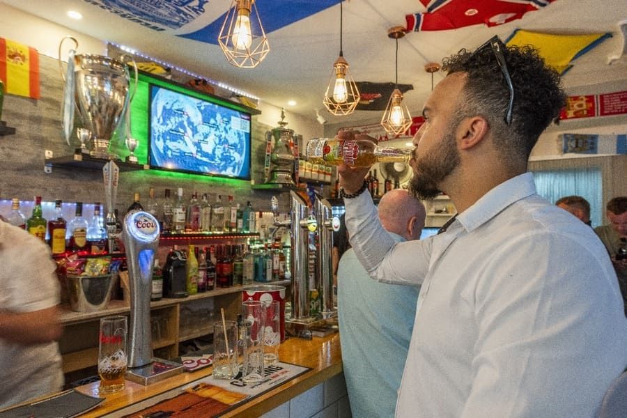 Un hombre está de pie en un bar bebiendo una cerveza.