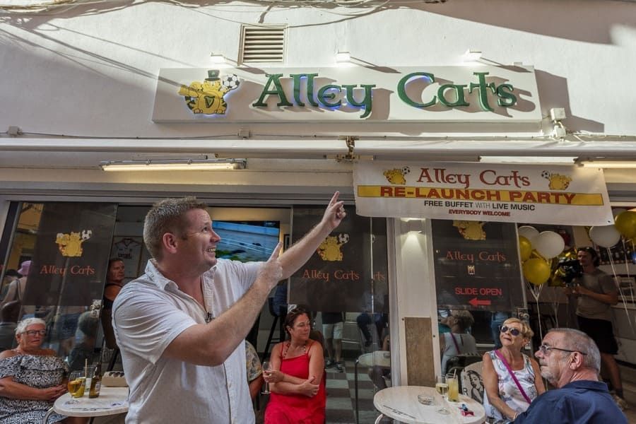Un hombre está parado frente a un restaurante hablando con un grupo de personas.