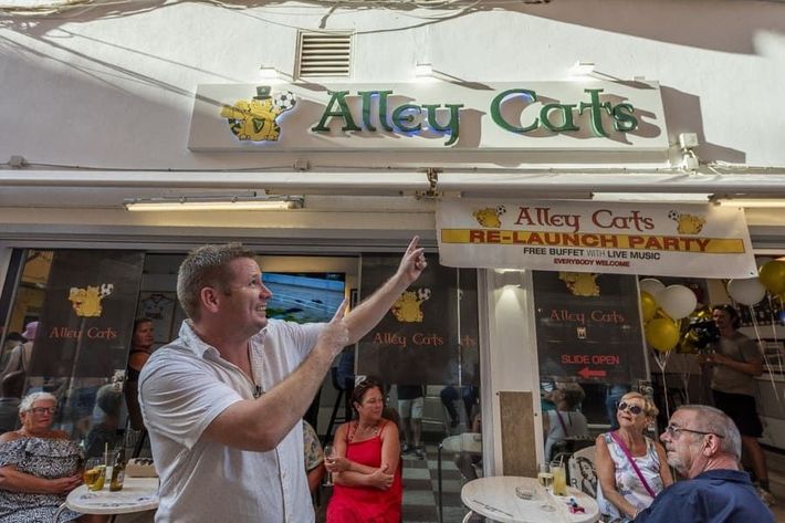 Un hombre está parado frente a un restaurante hablando con un grupo de personas.
