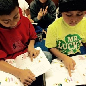 A boy wearing a mr lucky shirt is reading a book