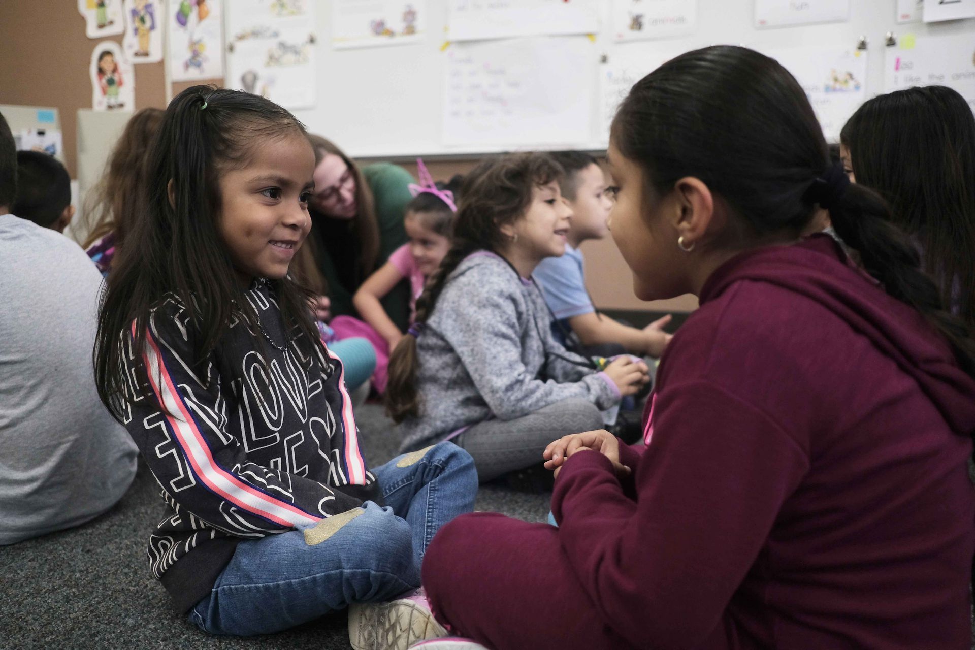 A group of children are sitting on the floor in a classroom talking to each other.