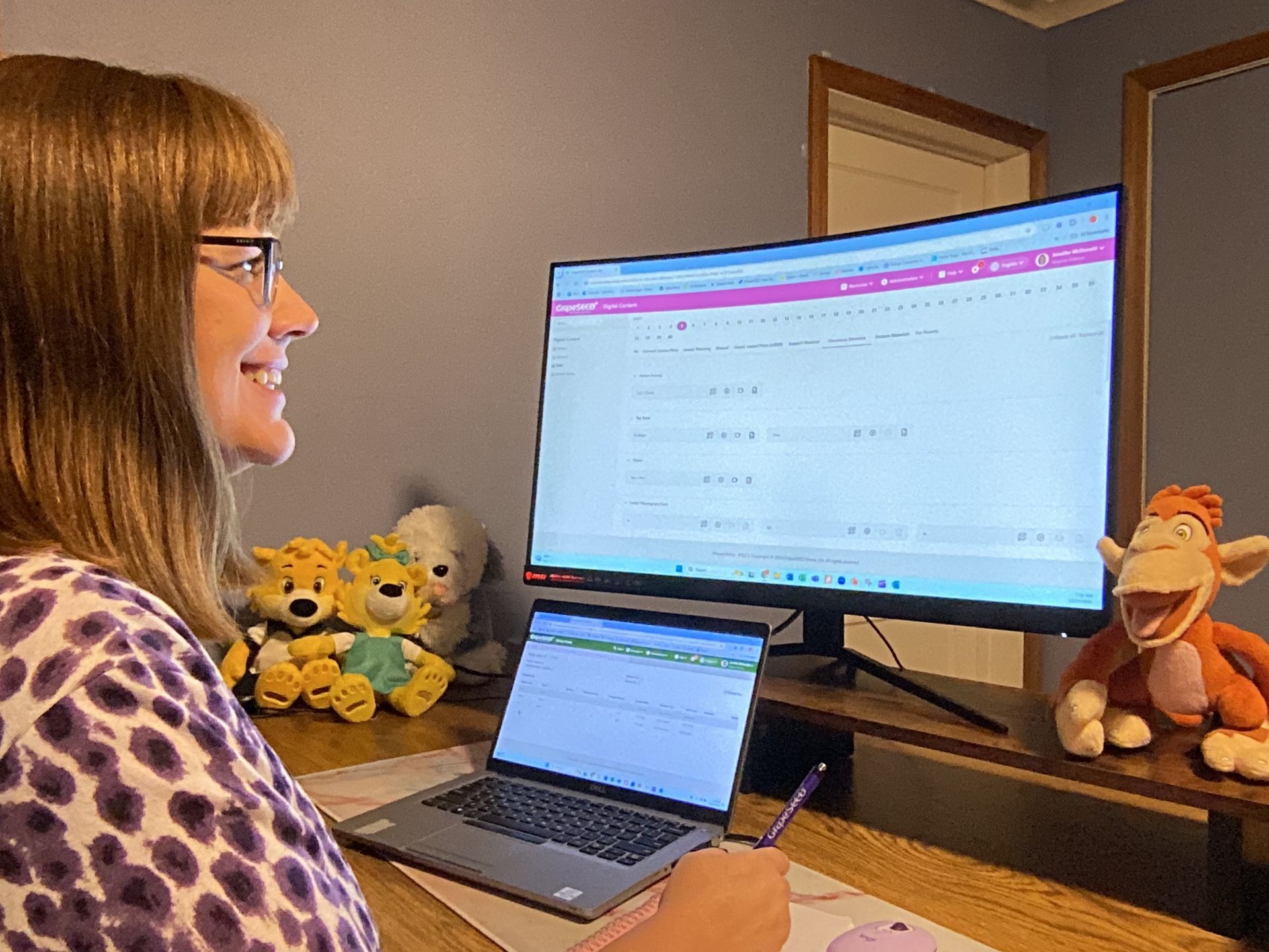 A woman is sitting at a desk with a laptop and a computer.