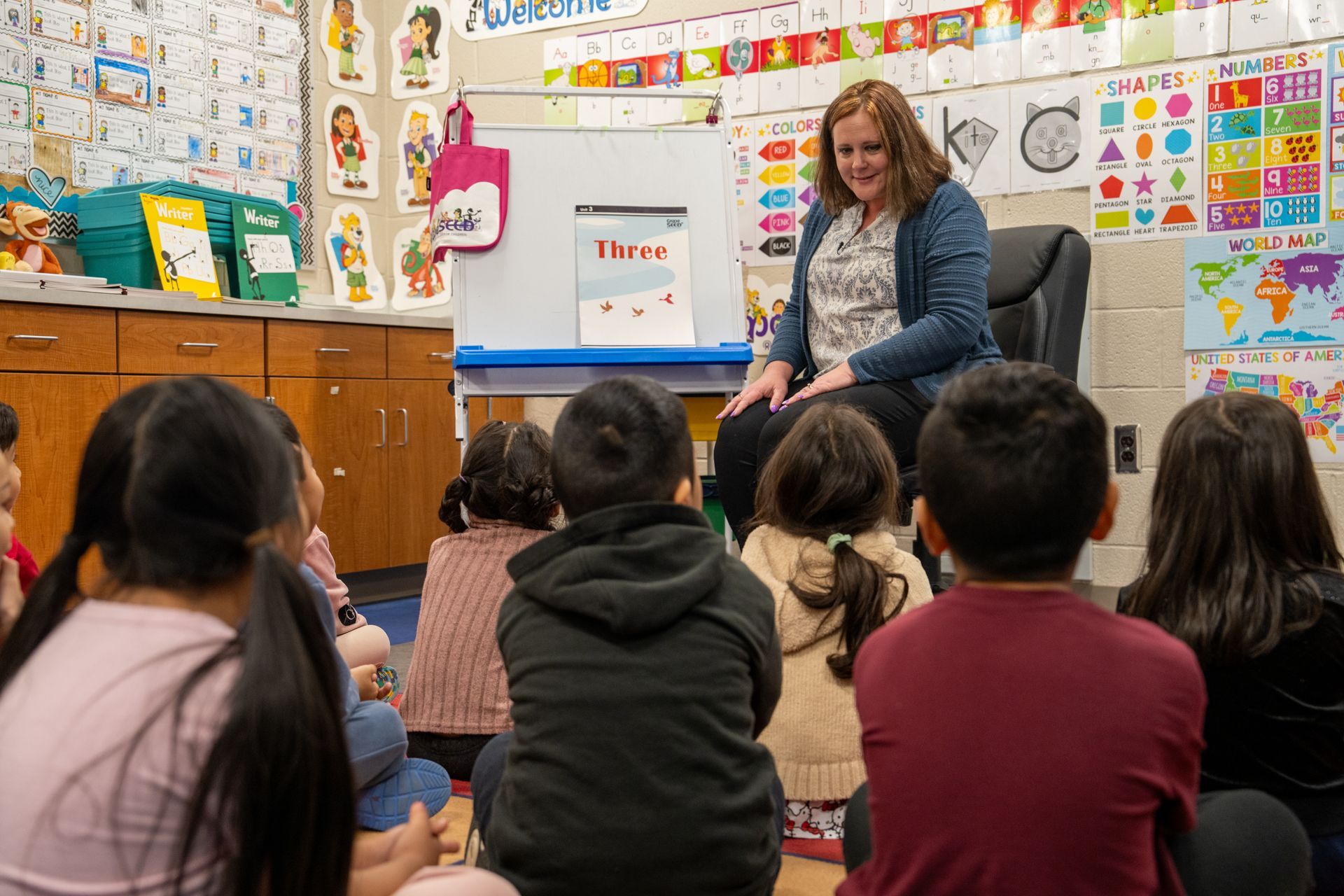 Teacher reads a book to a group of children in a colorful classroom.