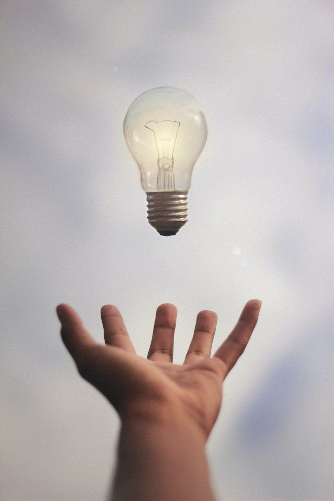 A hand is reaching for a light bulb in the sky.