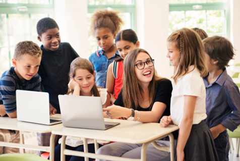 A teacher is teaching a group of children how to use a laptop computer.