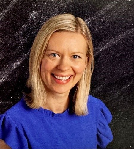 A woman in a blue shirt is smiling in front of a black background