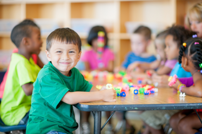 A boy in a green shirt is sitting at a table with other children.