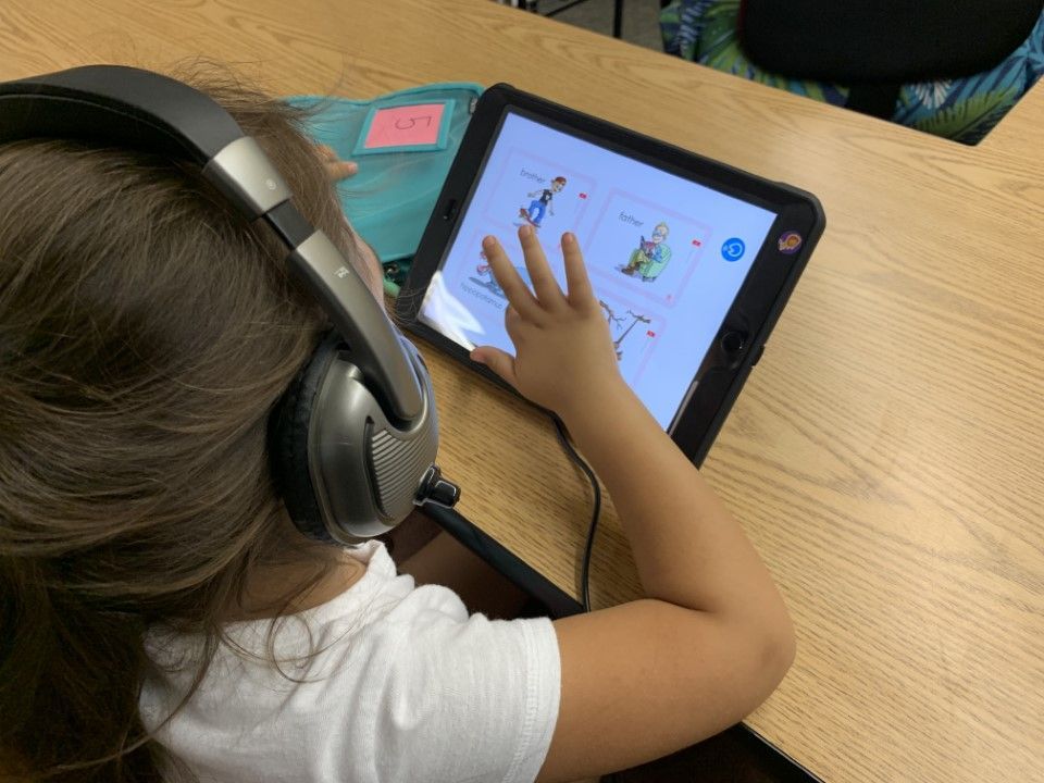 A little girl wearing headphones is using a tablet computer.