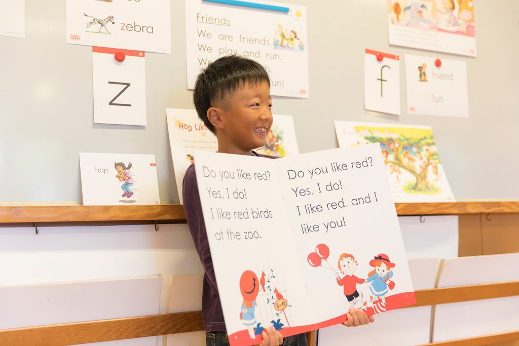 A young boy is holding a sign in front of a whiteboard.