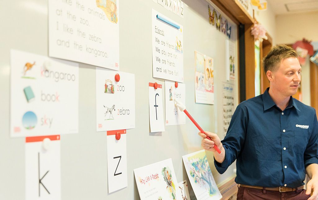 A man is pointing at a whiteboard in a classroom.