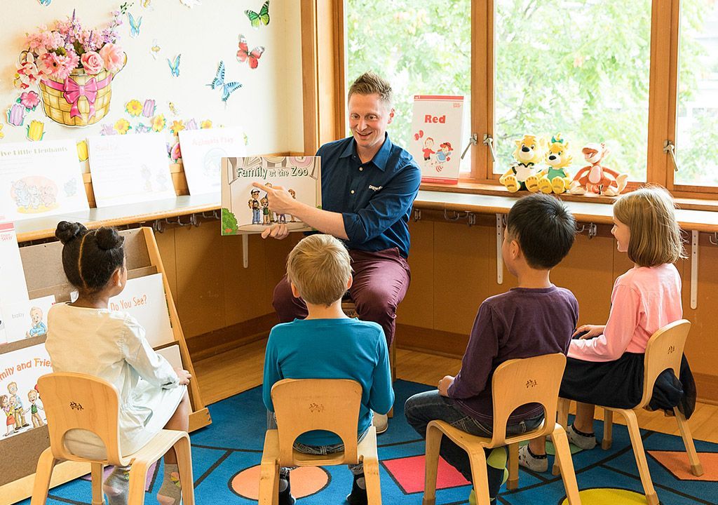 A man is reading a book to a group of children in a classroom.