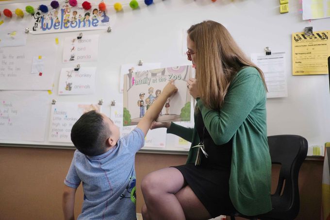 A teacher is reading a book to a young boy in a classroom.