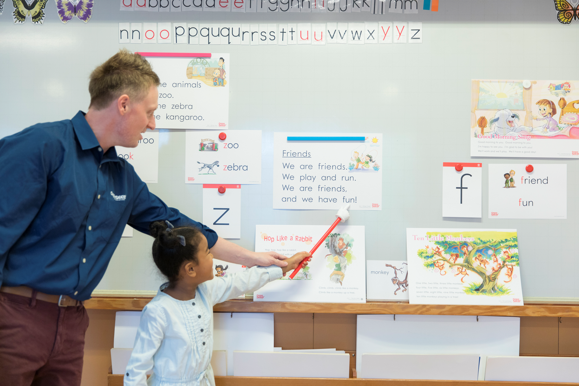 A man and a girl are standing in front of a whiteboard in a classroom.