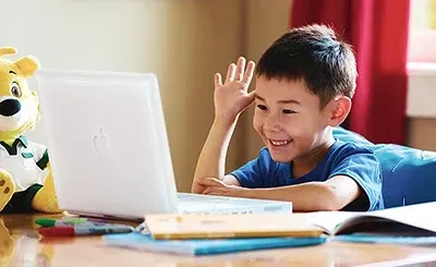 A young boy is sitting at a desk using a laptop computer.