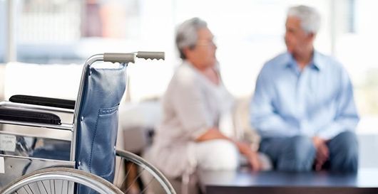 Un hombre y una mujer están sentados en una mesa con una silla de ruedas en primer plano.