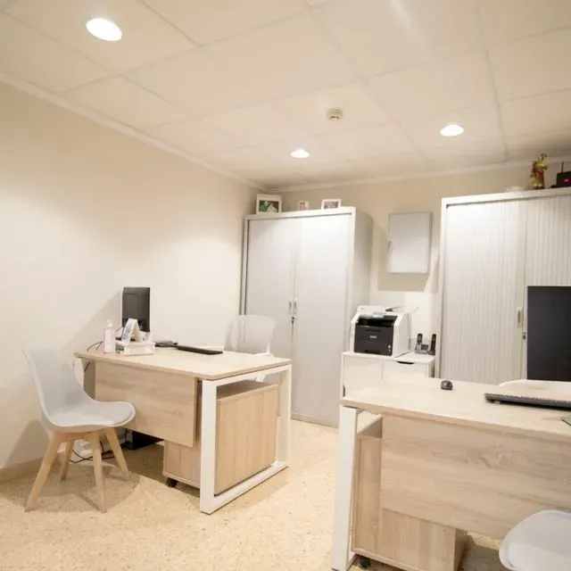 Una habitación con dos escritorios y sillas y una impresora.