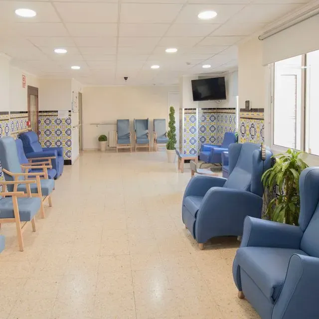 Una sala de espera con sillas azules y un televisor.