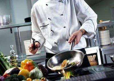 Un chef está cocinando verduras en una sartén en una cocina.