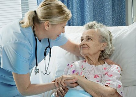 Una enfermera sostiene la mano de una anciana en una cama de hospital.