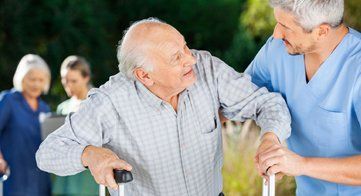 Un anciano está siendo ayudado por una enfermera con un andador.