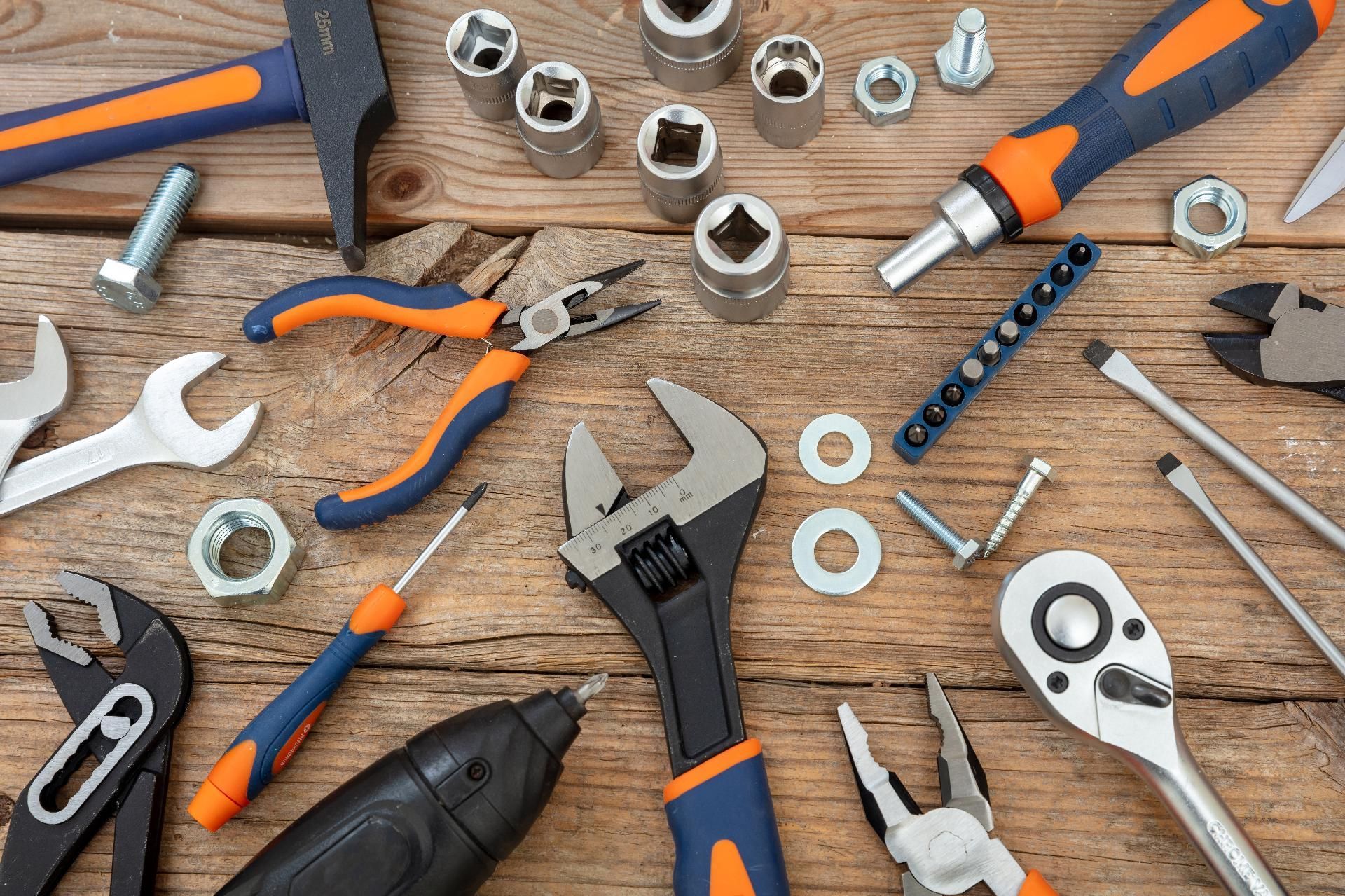 Handwerkzeuge Verschiedene Handwerkzeuge und Befestigungselemente mit orange-blauen Griffen lagen verstreut auf einer hölzernen Werkbank.