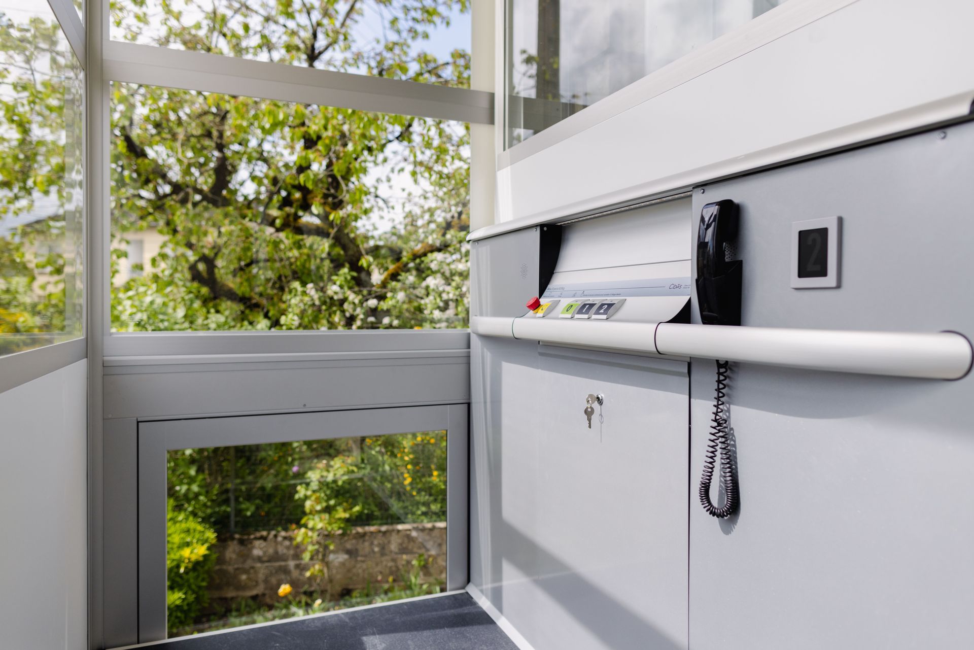 Un ascenseur privatif avec commandes et rampe. Vue sur les arbres depuis les fenêtres.