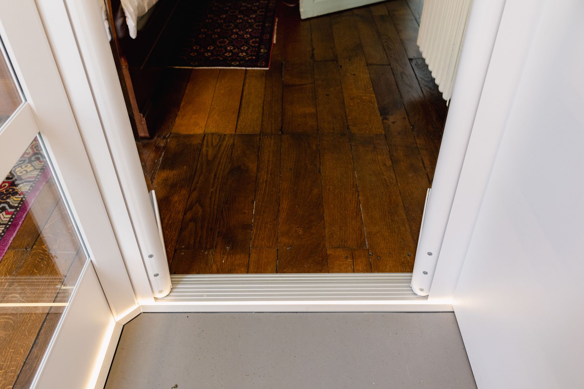 Porte avec seuil en aluminium, parquet et cadre de porte blanc.