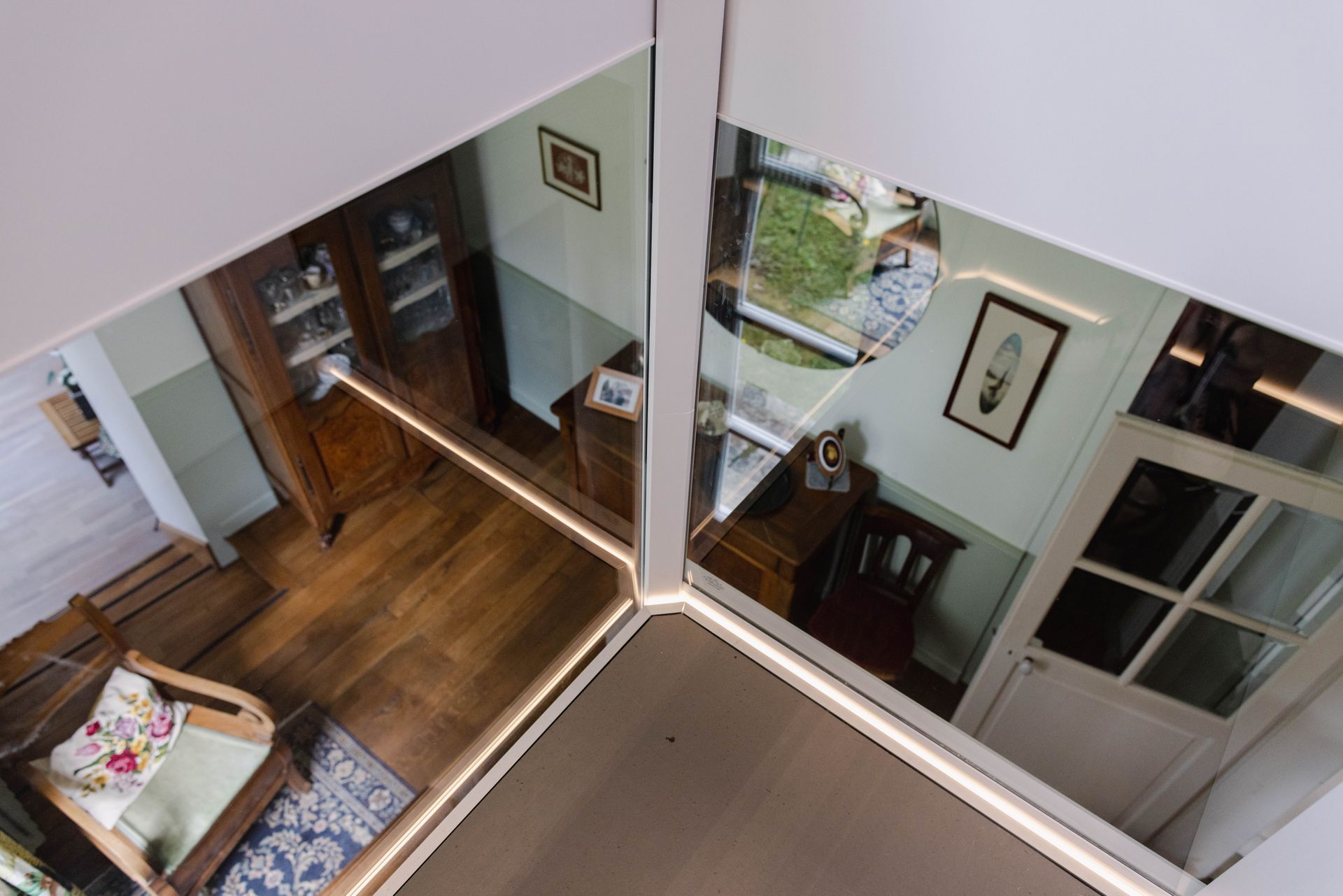 Vue aérienne de deux pièces avec parquet, meubles anciens et parois vitrées aux encadrements blancs.