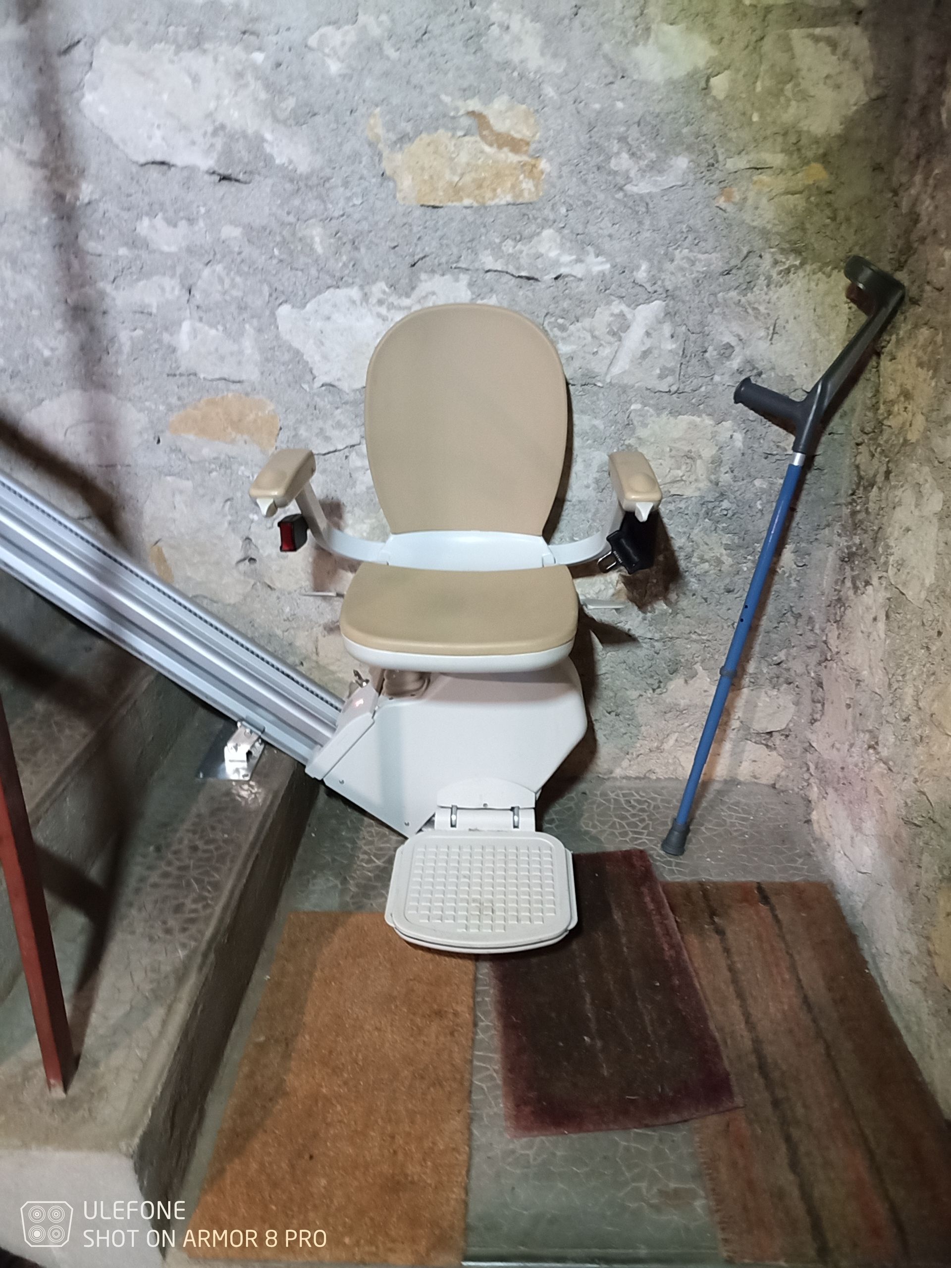 Un fauteuil monte-escalier sur un escalier en pierre, avec une paire de béquilles à proximité.