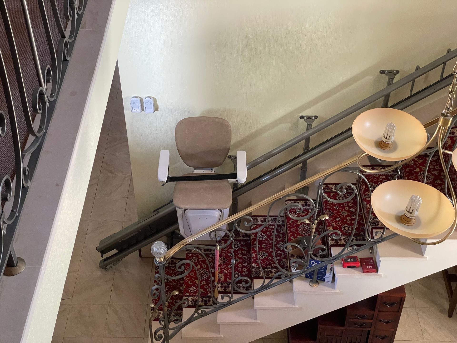 Monte-escalier dans un escalier. Chaise beige sur rails. Moquette beige et rouge sur les marches.