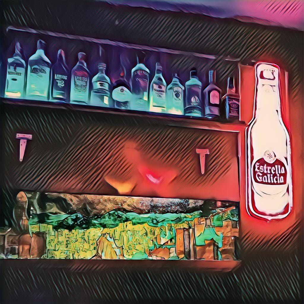 Estantería de bar con botellas de licor y cartel neón de Estrella Galicia.