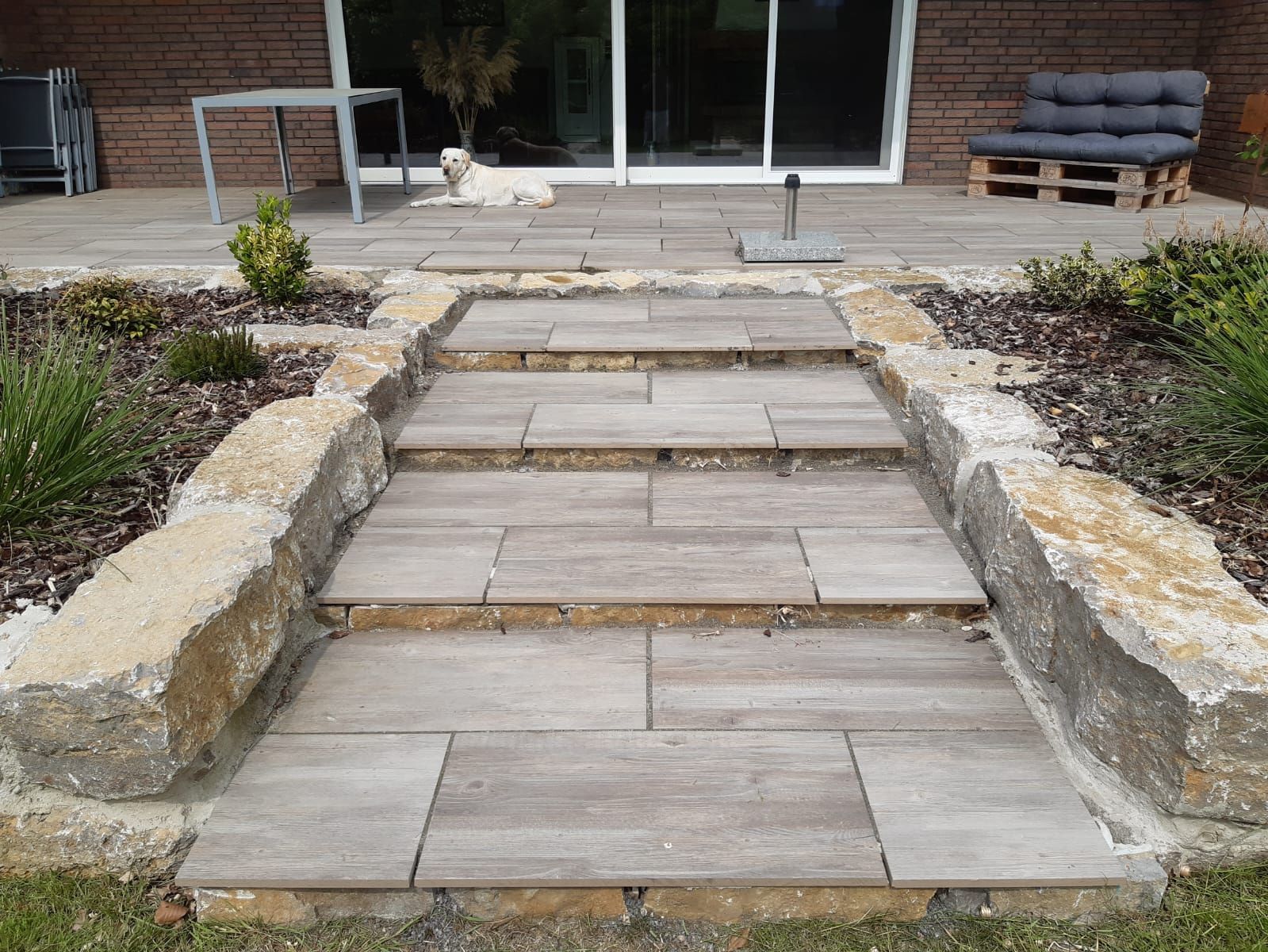 Ein Steinweg, der zu einer Terrasse führt, auf der ein Hund sitzt