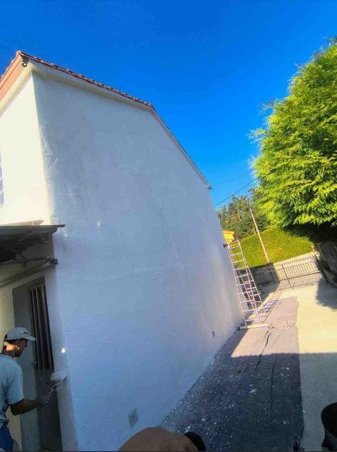 Obreros en un ascensor reparando un edificio de ladrillo con techo rojo. Una red verde cuelga debajo.