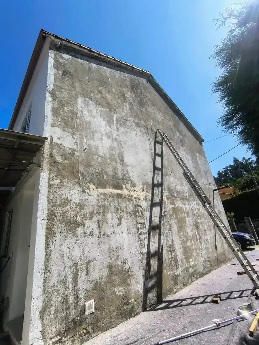 Obreros en un ascensor reparando un edificio de ladrillo con techo rojo. Una red verde cuelga debajo.