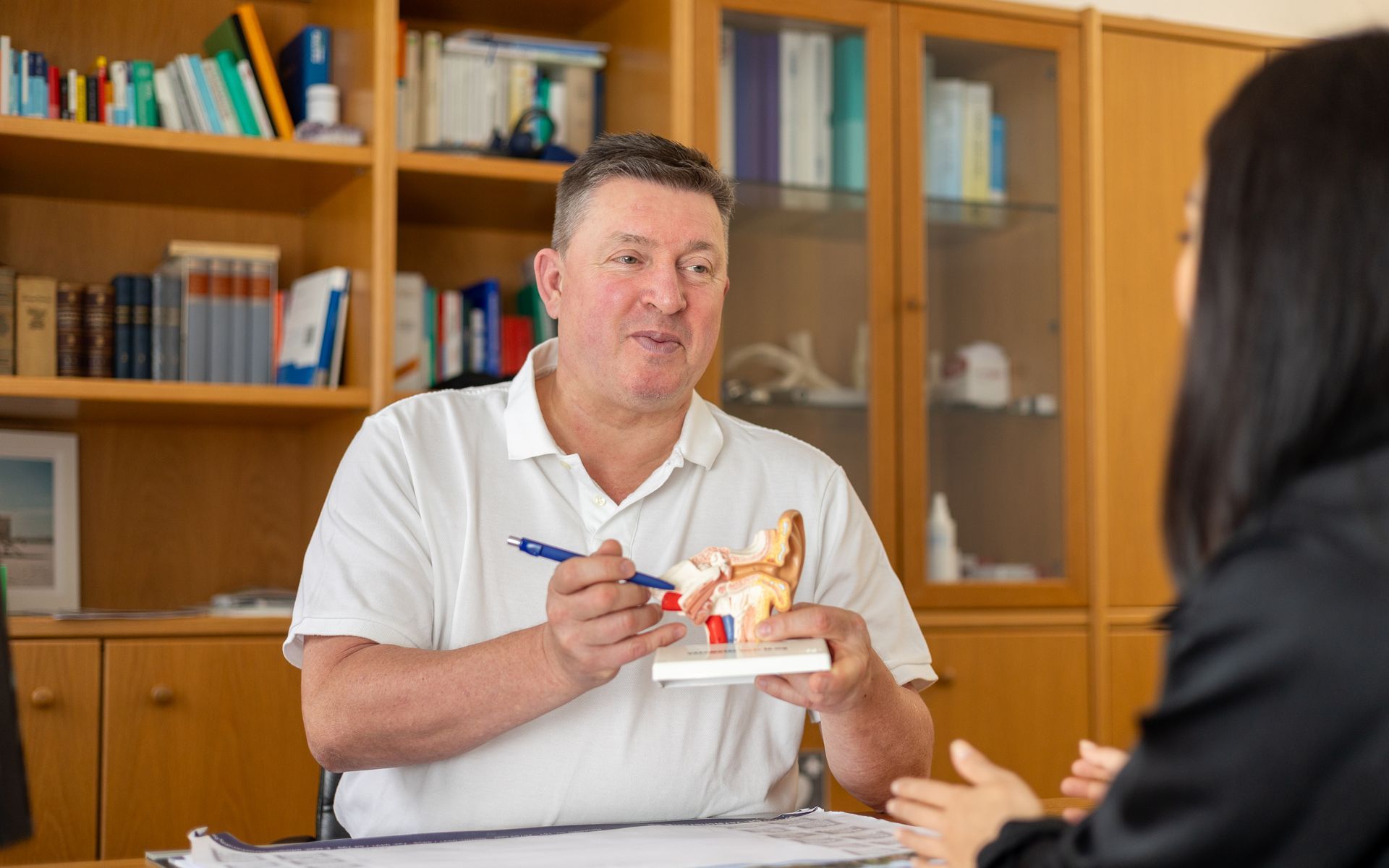 Ein Mann sitzt an einem Tisch, während er ein Modell eines menschlichen Ohrs in der Hand hält.