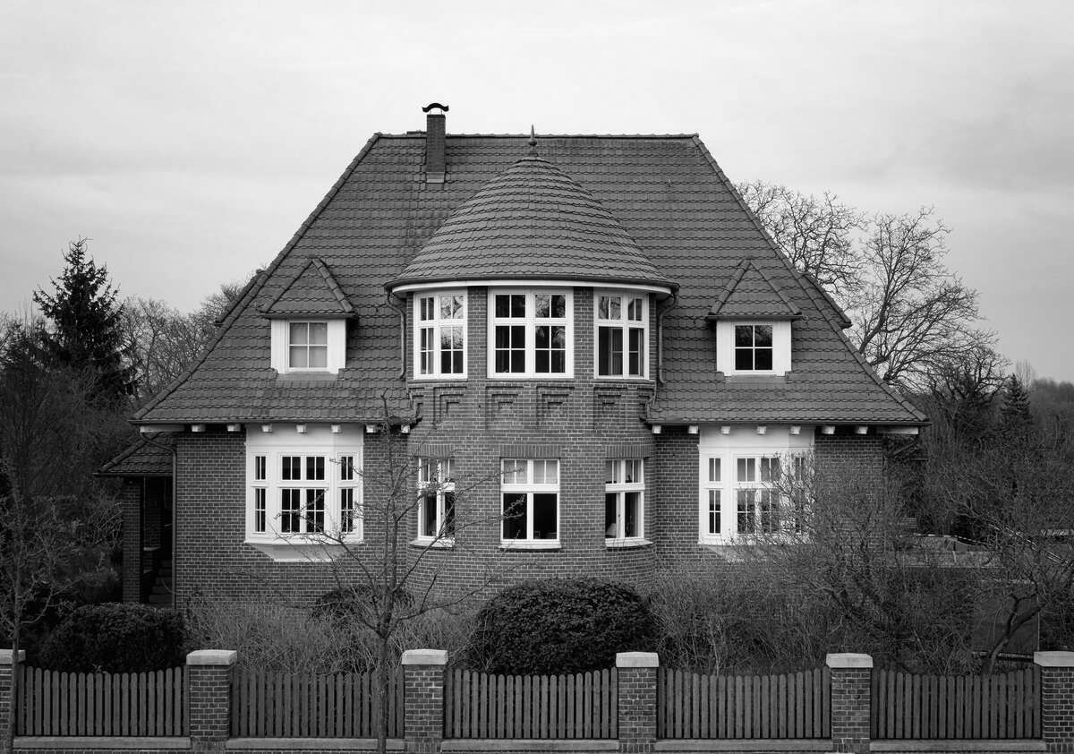 Ein Schwarzweißfoto eines großen Hauses mit einem Zaun darum herum.