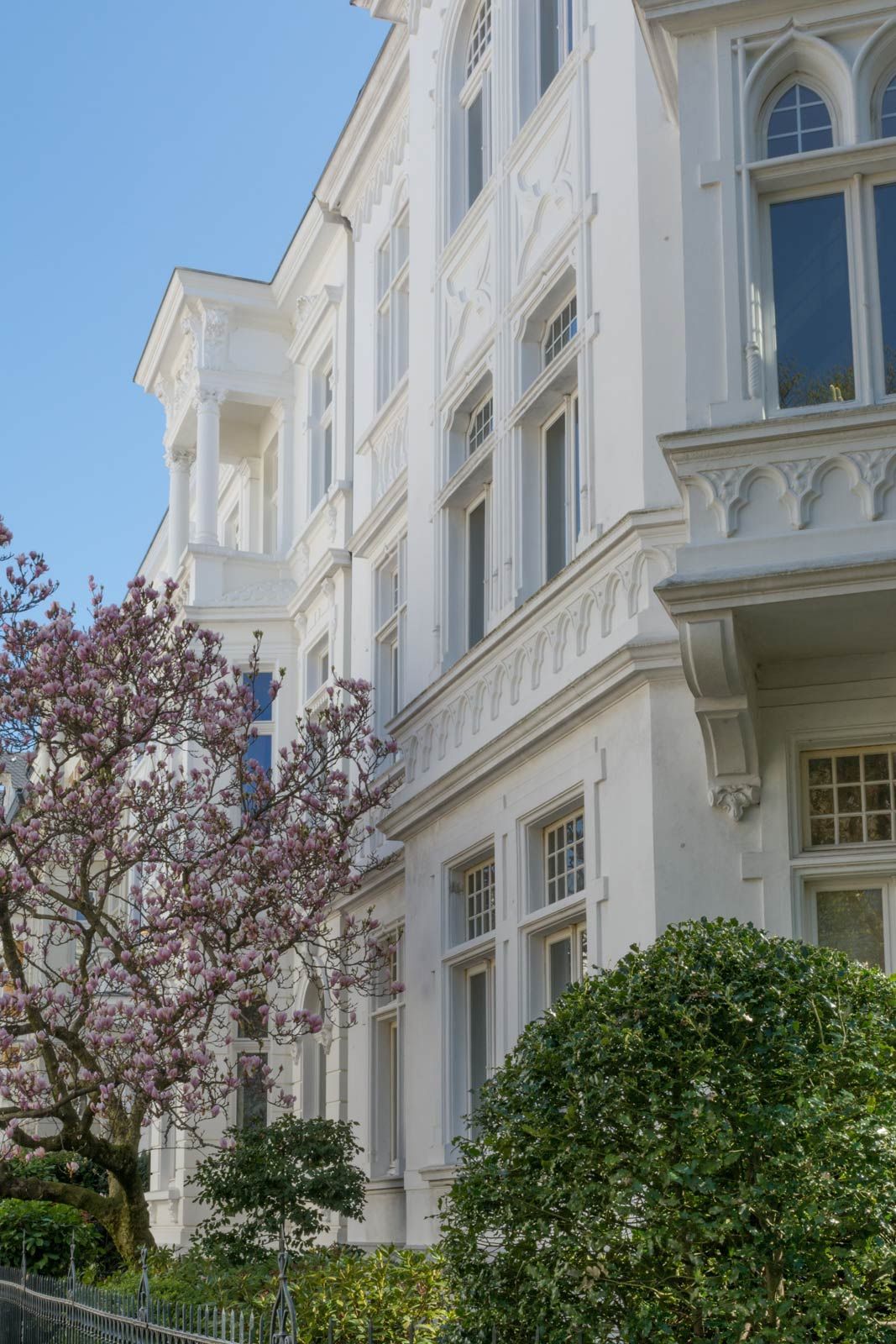 Ein großes weißes Gebäude mit einem Balkon und einem Baum davor.
