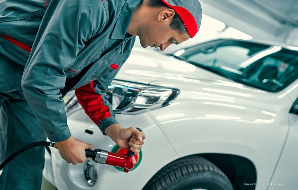 Ein Mechaniker poliert in einer Garage ein weißes Auto mit einer roten Poliermaschine.