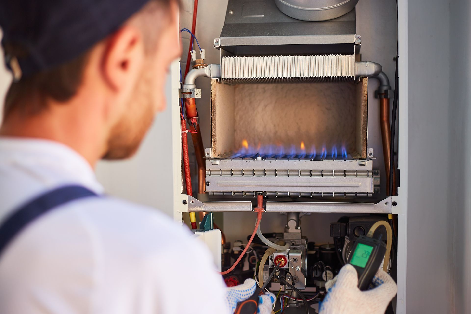 Un technicien inspecte une chaudière à gaz avec un appareil de mesure portatif ; des flammes bleues sont visibles à l'intérieur.