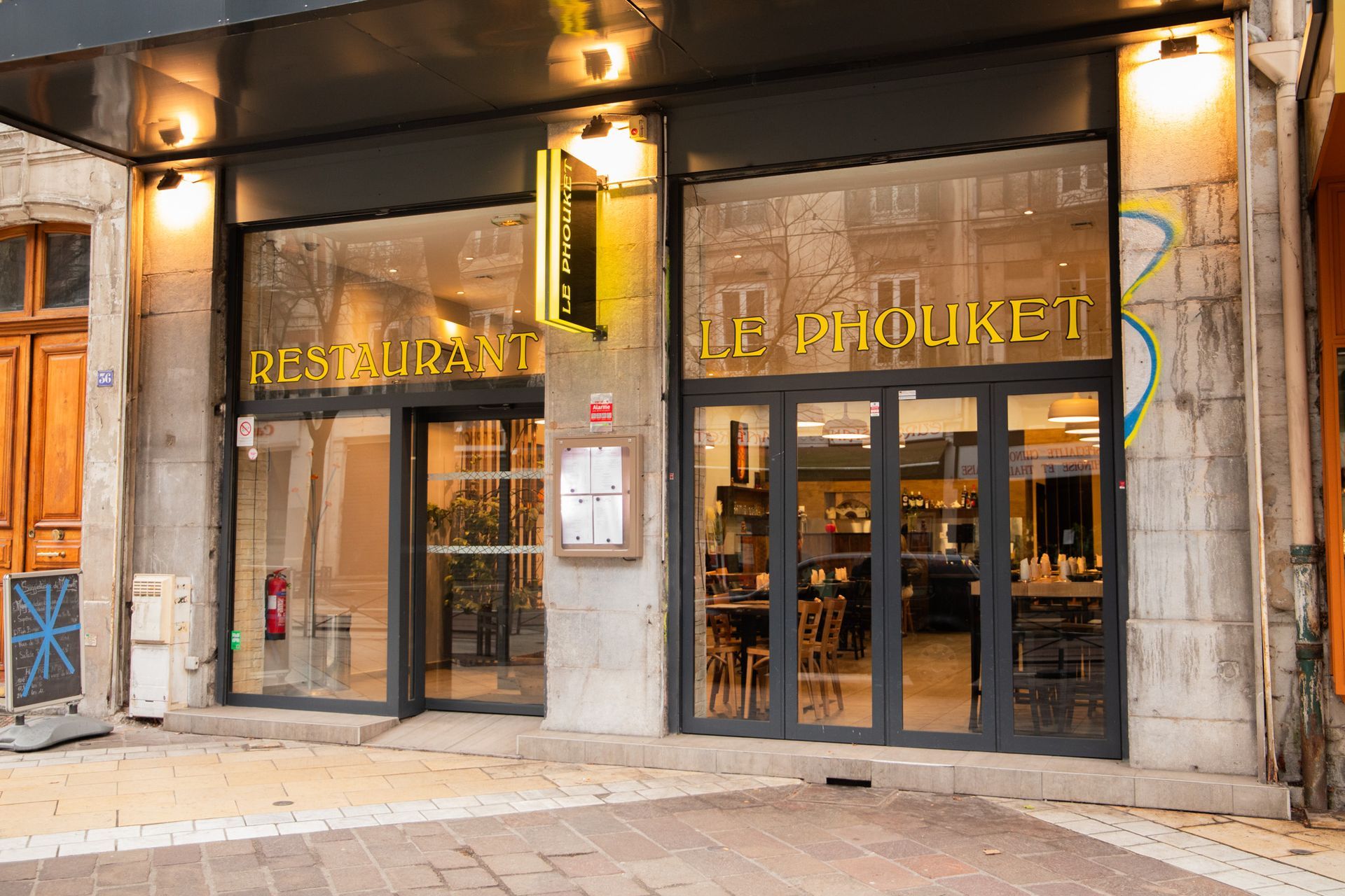 Extérieur du restaurant « Le Bouket » : portes vitrées, enseigne jaune, façade en pierre.