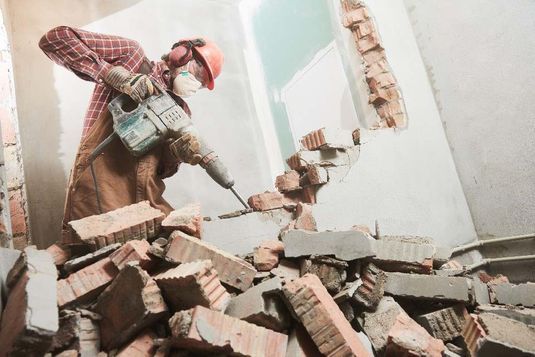 Mann in Schutzkleidung reißt Wand ein