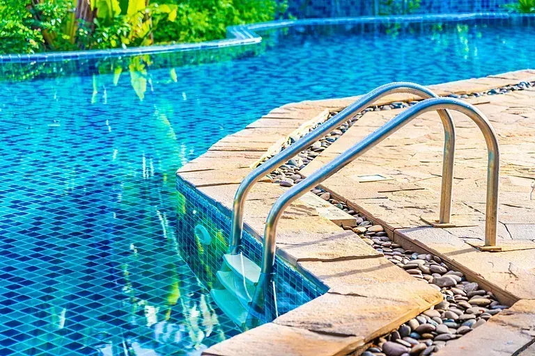 Una piscina con escaleras que conducen a ella y un reflejo de árboles en el agua.