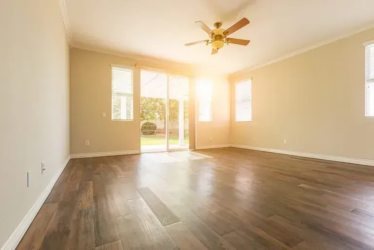 Una sala de estar vacía con pisos de madera y un ventilador de techo.