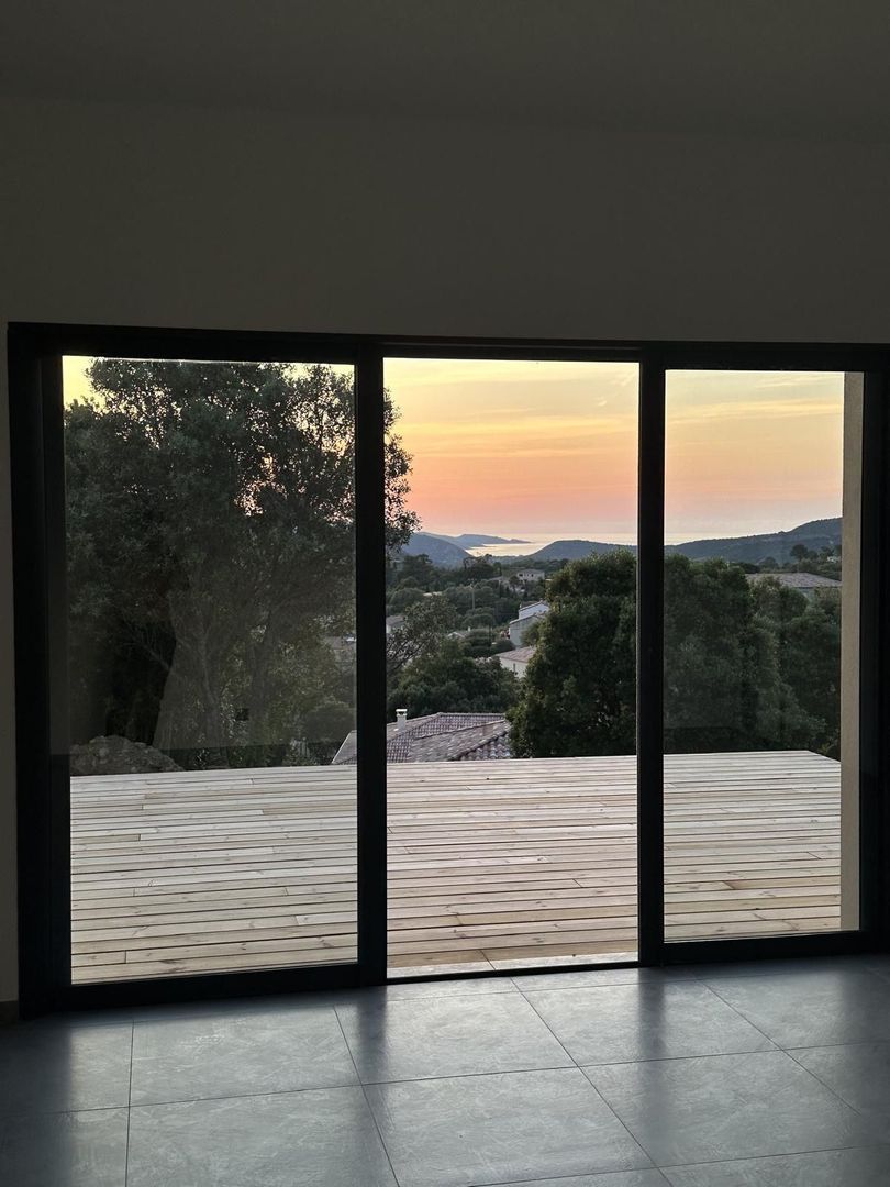 Des portes coulissantes en verre s'ouvrent sur une vue du coucher de soleil sur les collines et les arbres, sol carrelé à l'intérieur.